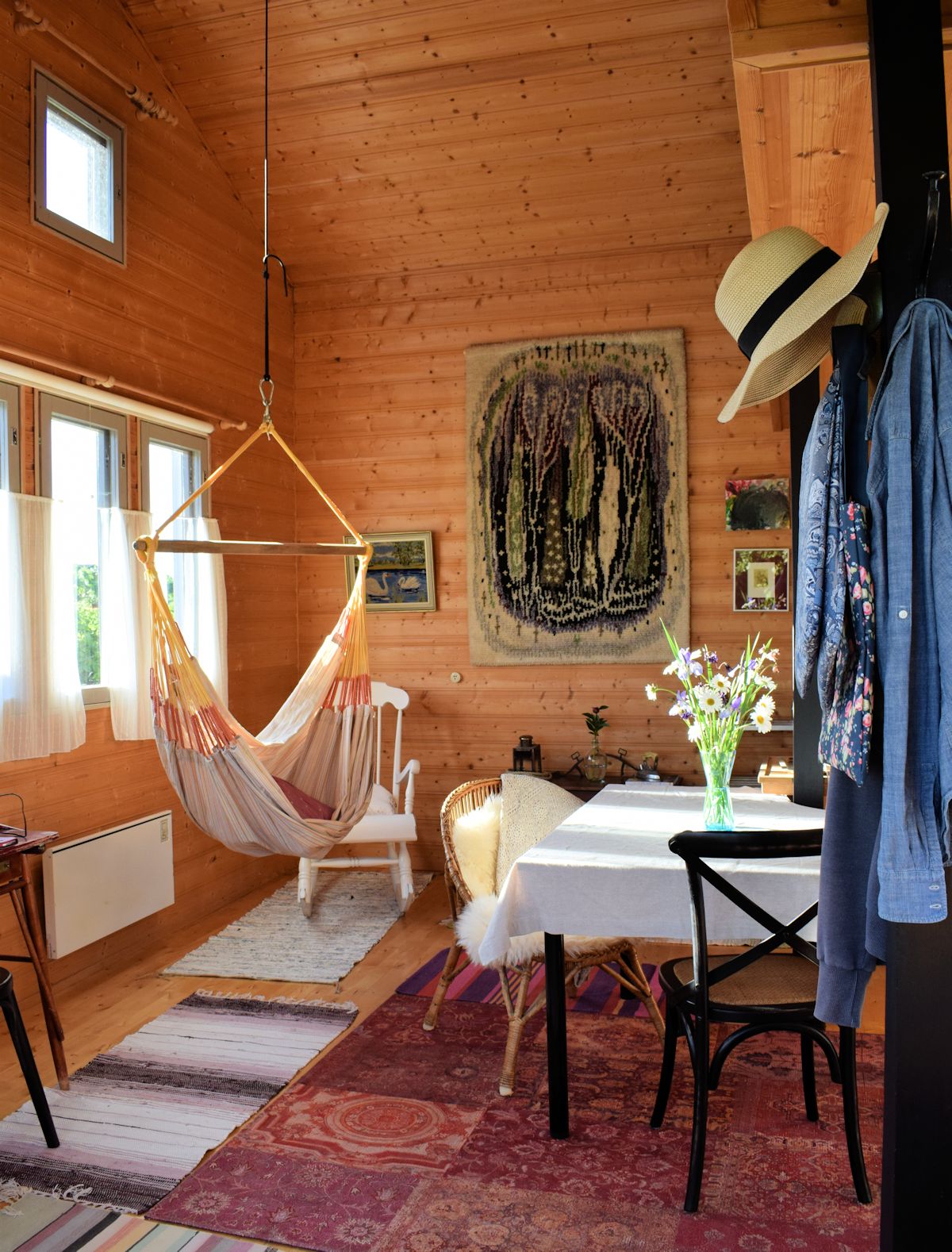 Siirtolapuutarhamökki sisältä. Mäntypaneelia, patchwork-matto, riipputuoli sisällä.